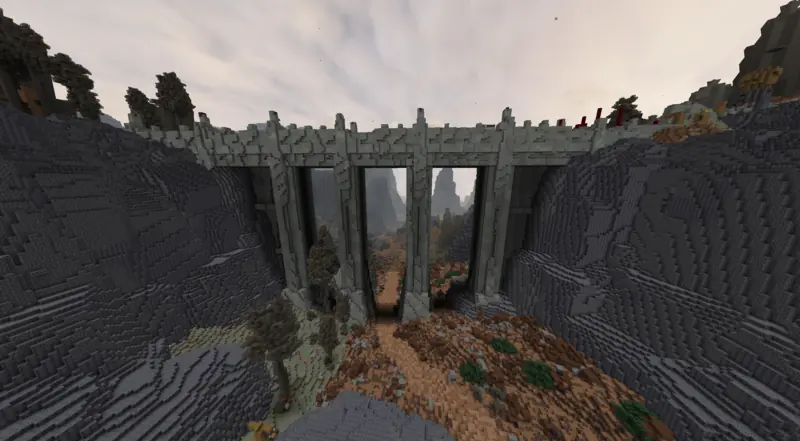 a tall arched stone bridge spanning a rocky canyon, dry trees below